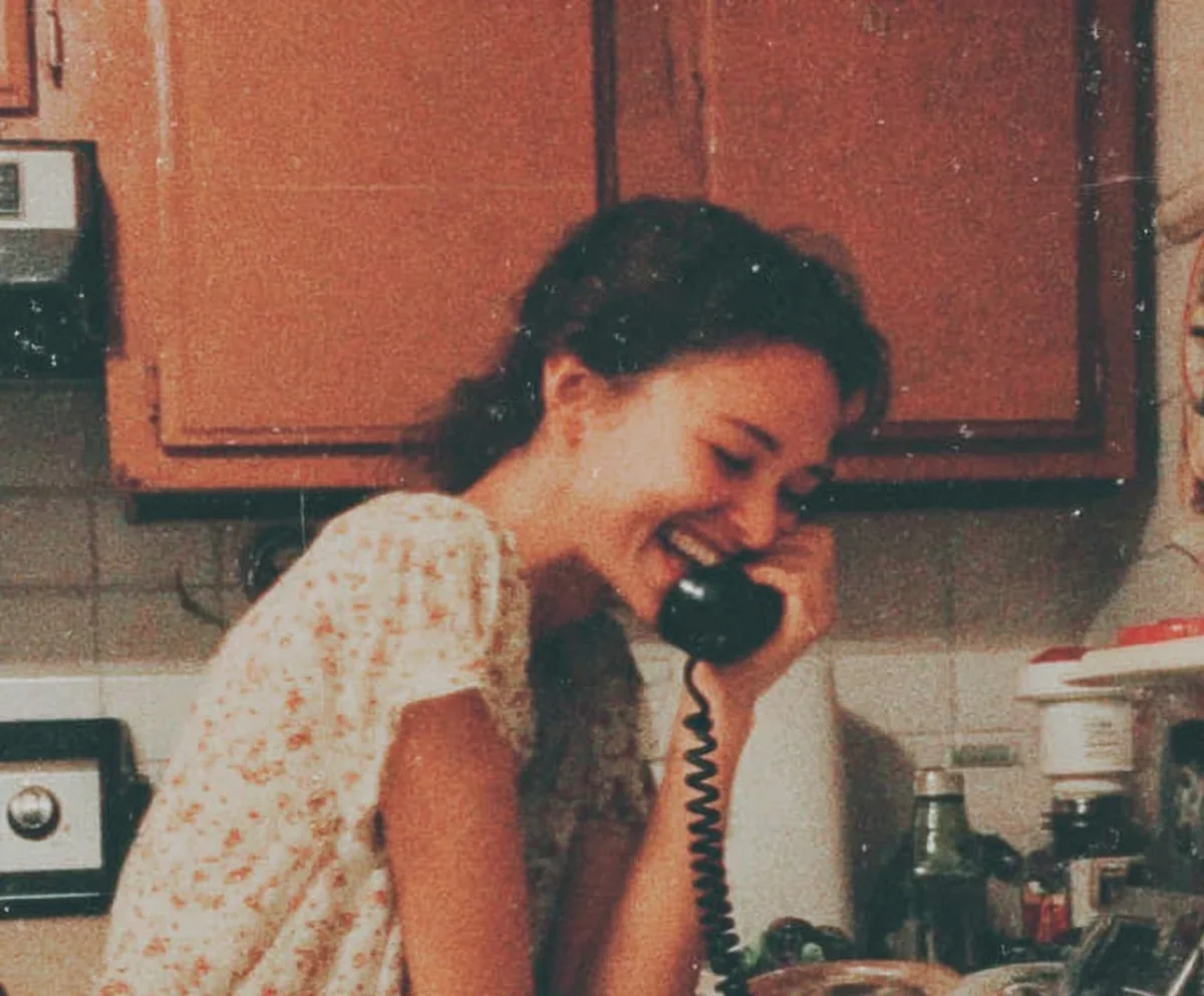 Mujer mayor sonriendo mientras habla por teléfono junto a la ventana